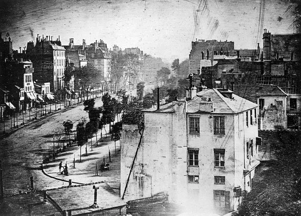 Louis Daguerre:  Boulevard du Temple, Paris, 3. Arrondissement )1838) Daguerreotype. Believed to be the earliest photograph showing a living person. It is a view of a busy street, but because the exposure time was at least ten minutes the moving traffic left no trace. Only the two men near the bottom left corner, one apparently having his boots polished by the other, stayed in one place long enough to be visible. Note that, as with most daguerreotypes, the image is a mirror image.